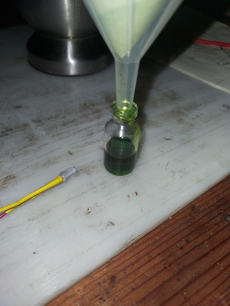 Finished green solution in small glass container.