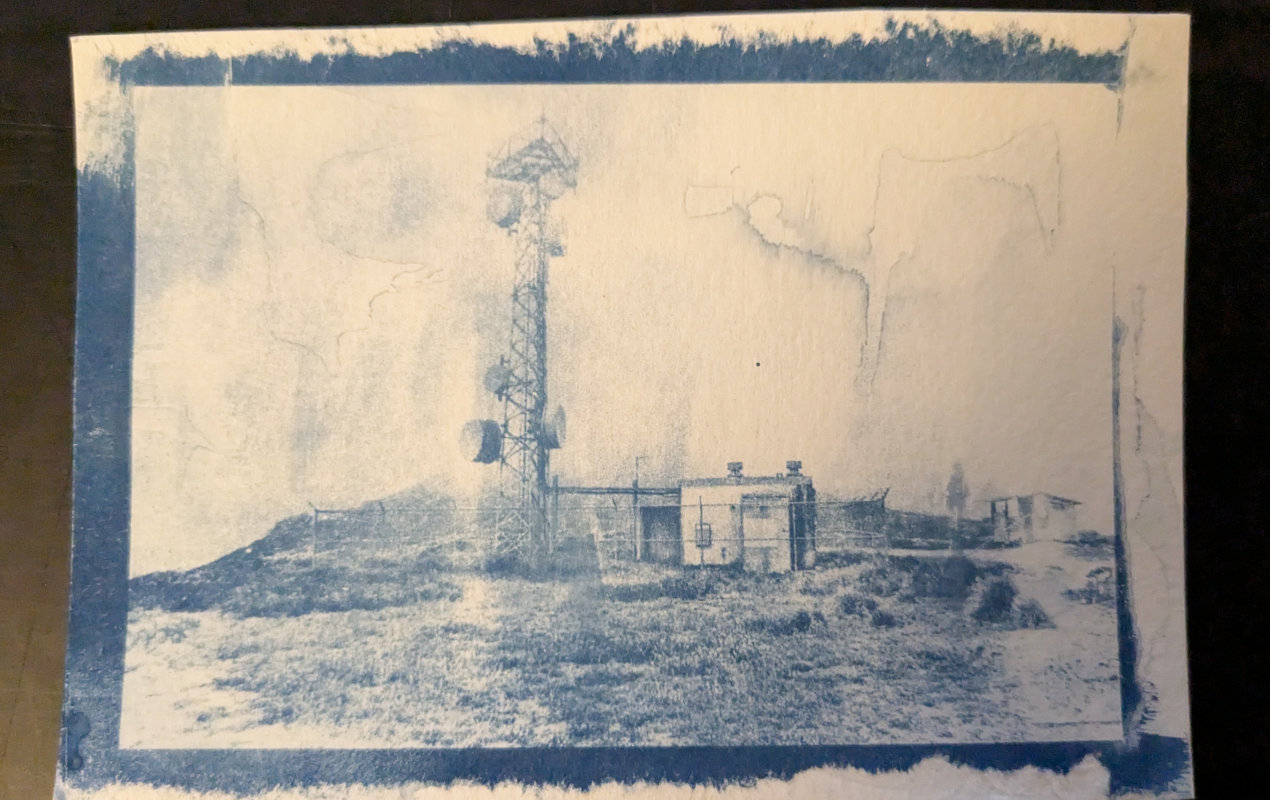 Blue-on-white photo of a microwave tower on a hill